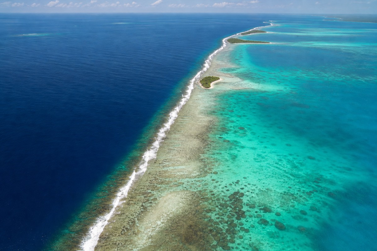 Aerial view of the Belize Barrier Reef, a white line of breaking surf separating pale shallow lagoon from deep blue Caribbean water