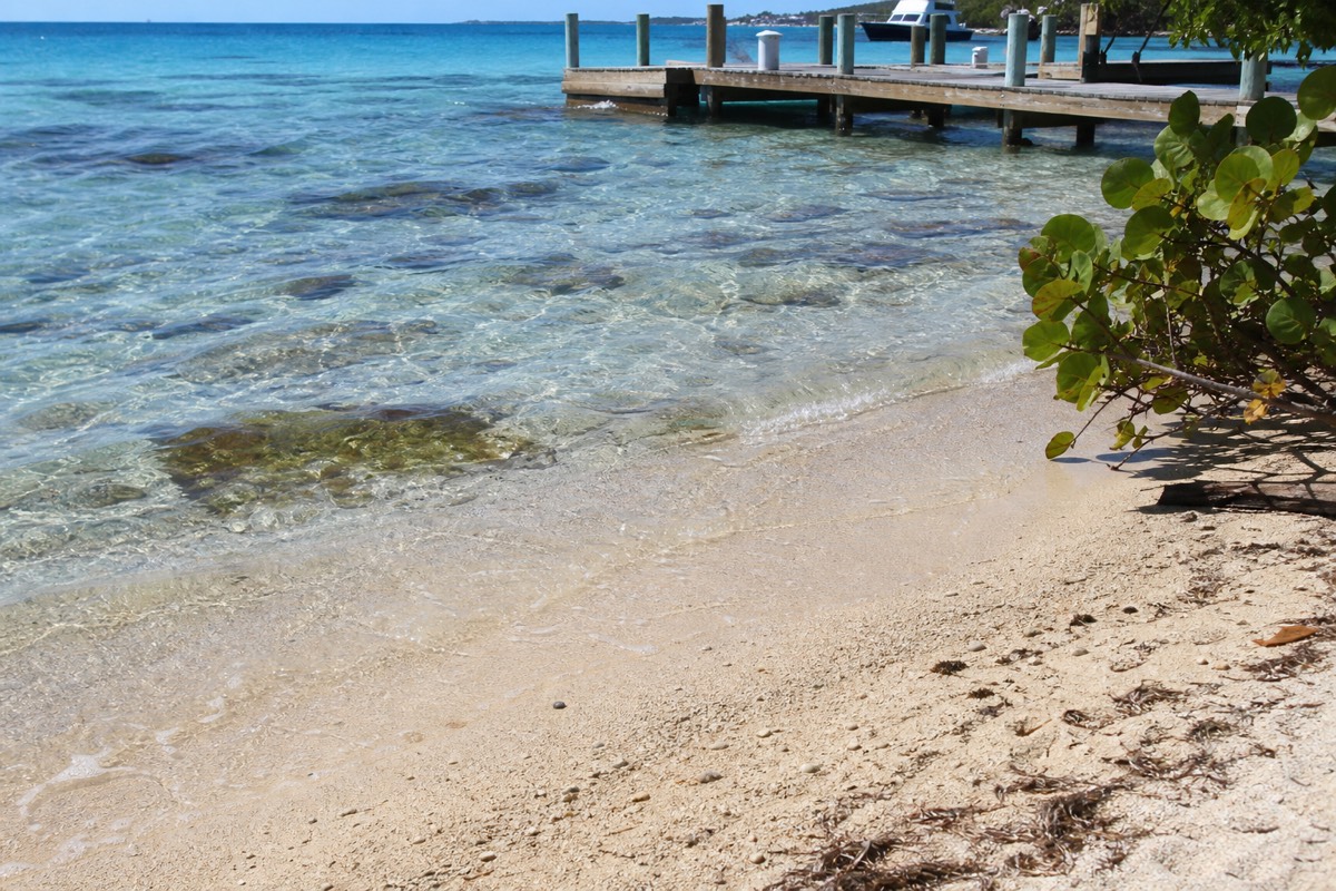 Shallow turquoise water and a dock on a Belize caye, with the barrier reef breaking in the distance