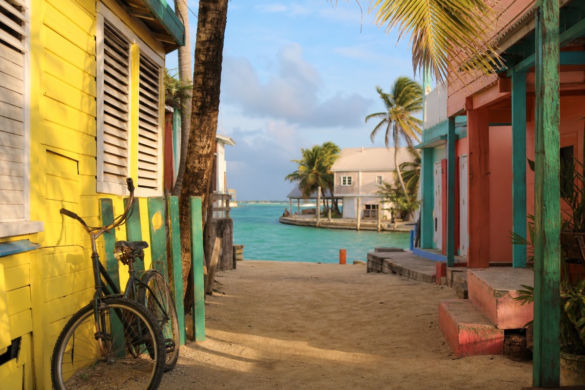 A snorkeling boat leaving the sandy waterfront at Caye Caulker, Belize, with shallow turquoise water and wooden docks