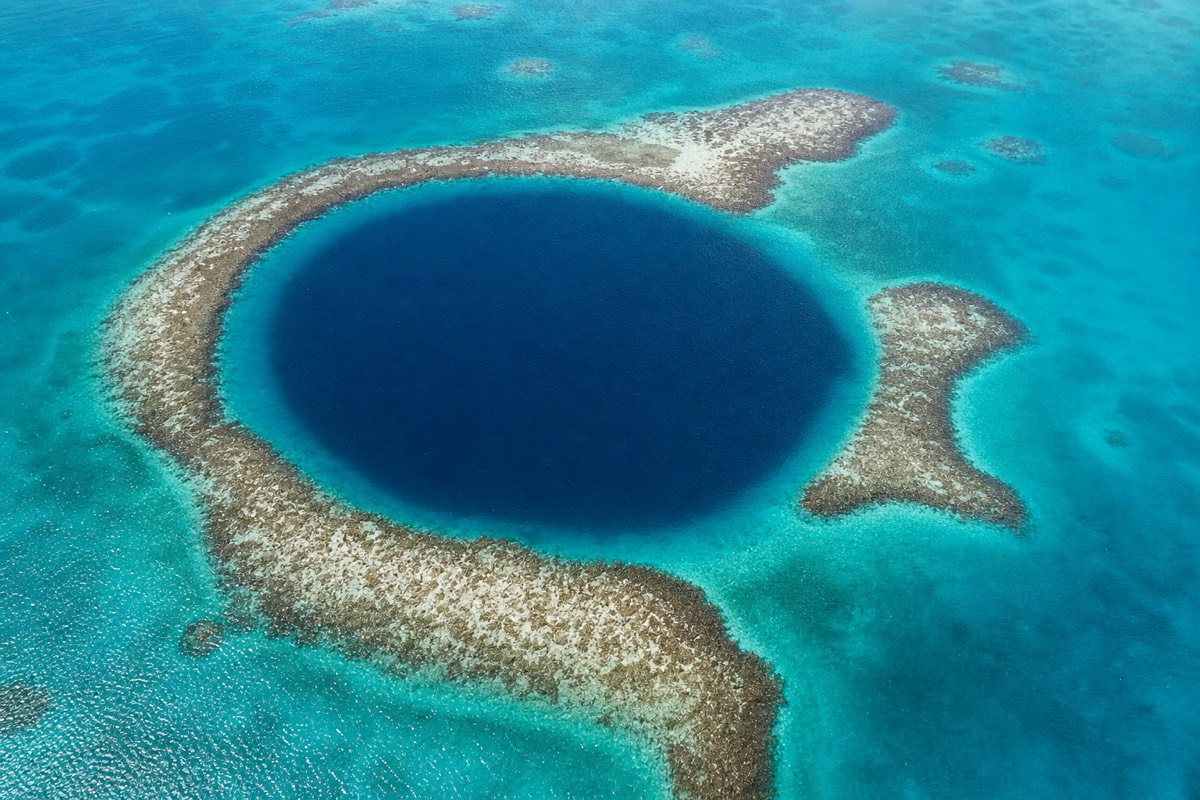 Aerial view of the Great Blue Hole, a dark circular sinkhole ringed by pale shallow reef inside Lighthouse Reef Atoll in Belize